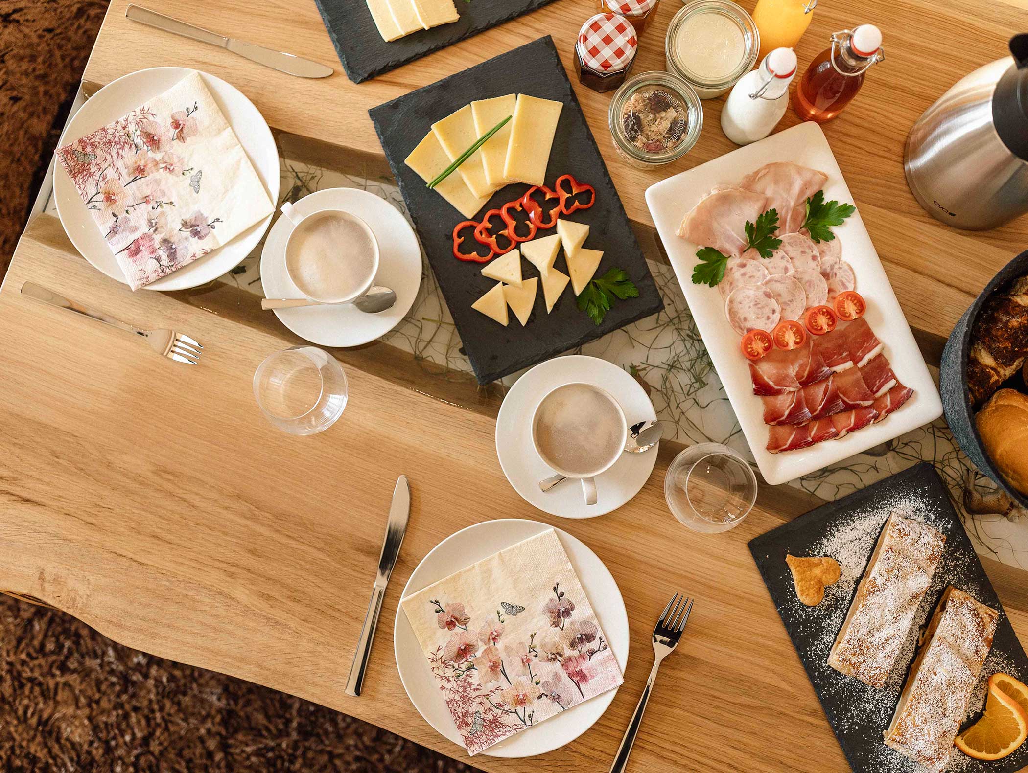 Frühstückstisch mit Kaffee, Aufschnitt, Käse, Gebäck und Saft, gedeckt mit Servietten und Besteck. - Langfennhof