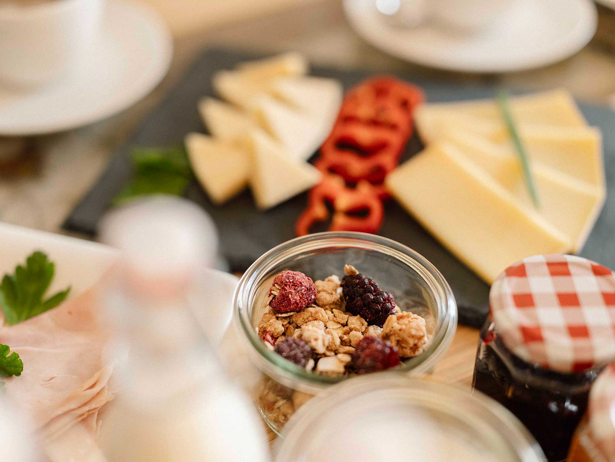 Eine Nahaufnahme eines Frühstücksaufstrichs mit Müsli, Käsescheiben, roter Paprika und einem Glas Marmelade. - Langfennhof