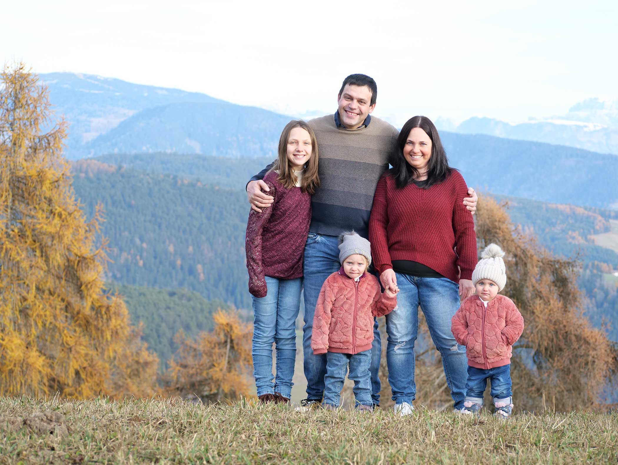 Eine fünfköpfige Familie posiert im Freien mit Herbstbäumen und Bergen im Hintergrund. - Langfennhof