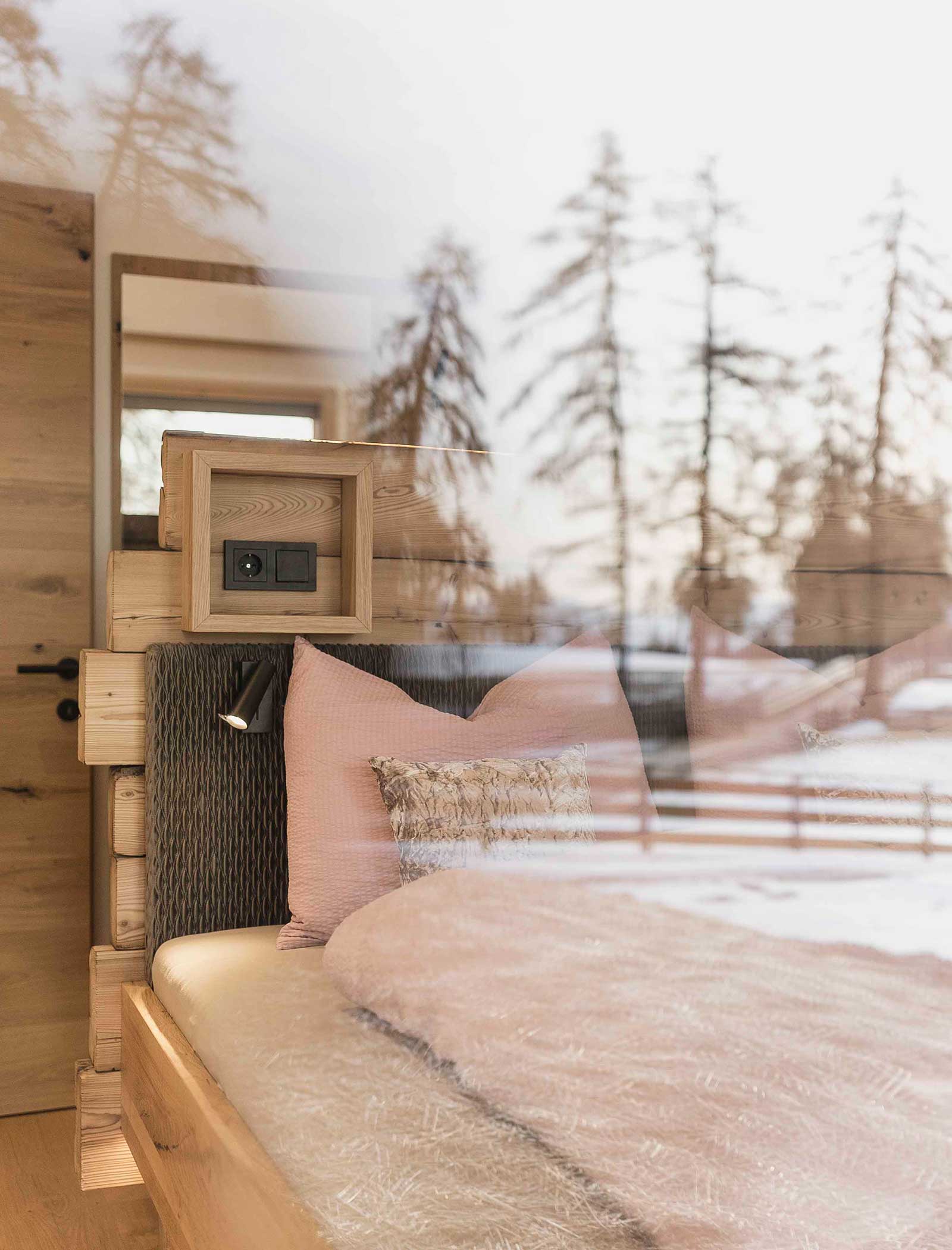 Gemütliches Holzschlafzimmer mit rosafarbenem Bettzeug, Spiegelfenster mit Blick auf verschneite Bäume und Winterlandschaft draußen. - Langfennhof