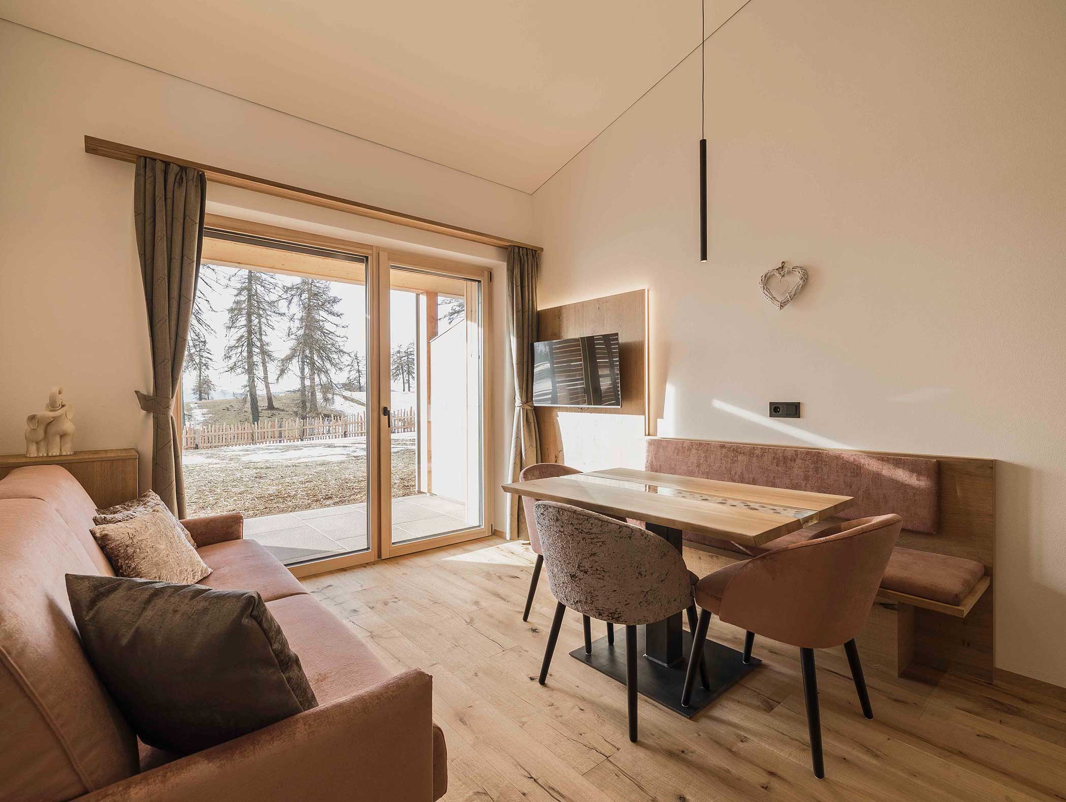 Moderner Wohn- und Essbereich mit Sofa, Tisch, Stühlen, TV, großen Fenstern und Blick auf die Bäume draußen. - Langfennhof