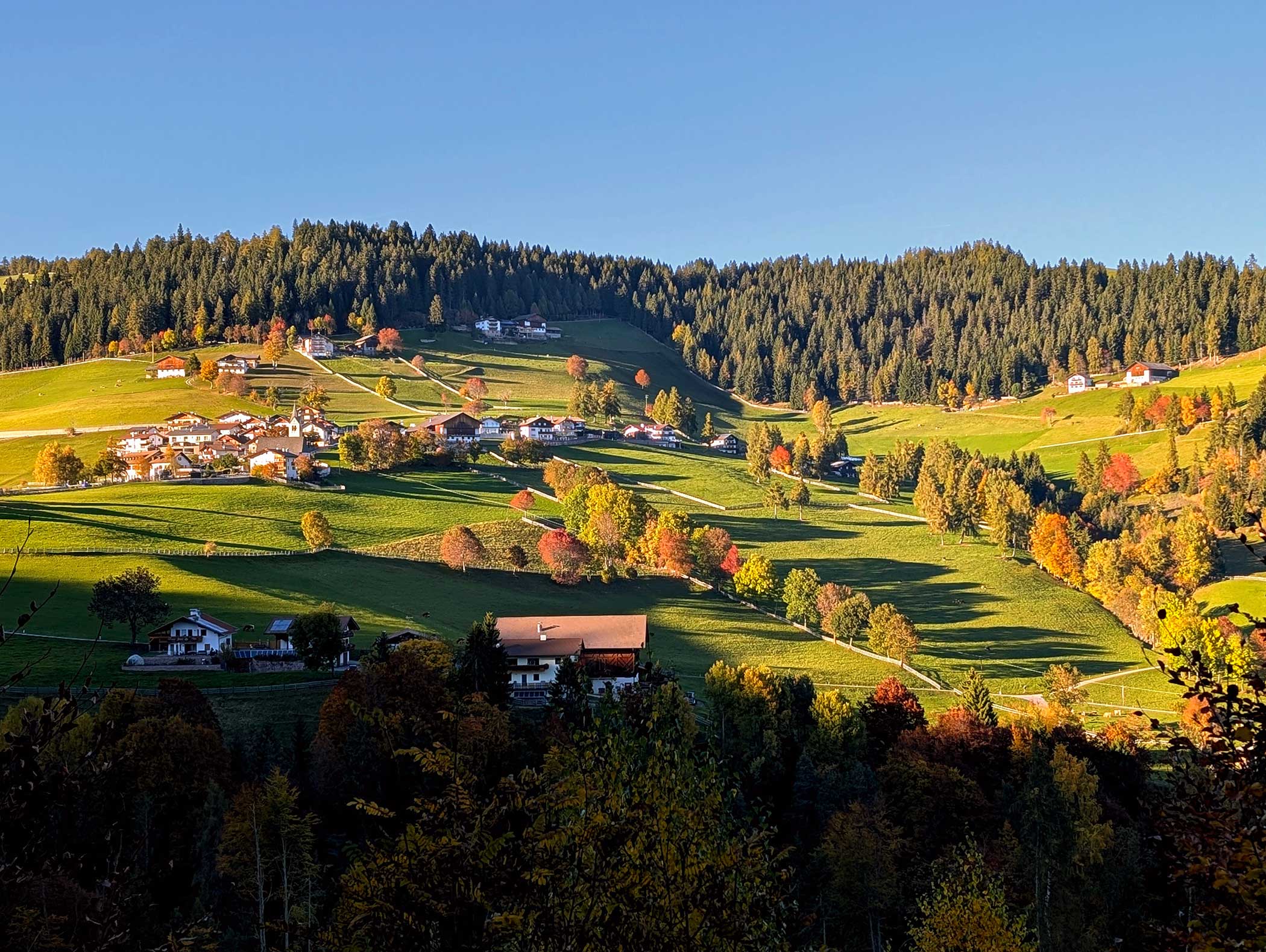 Eine sonnenbeschienene ländliche Landschaft mit sanften grünen Hügeln, verstreuten Häusern und bunten Herbstbäumen. - Langfennhof