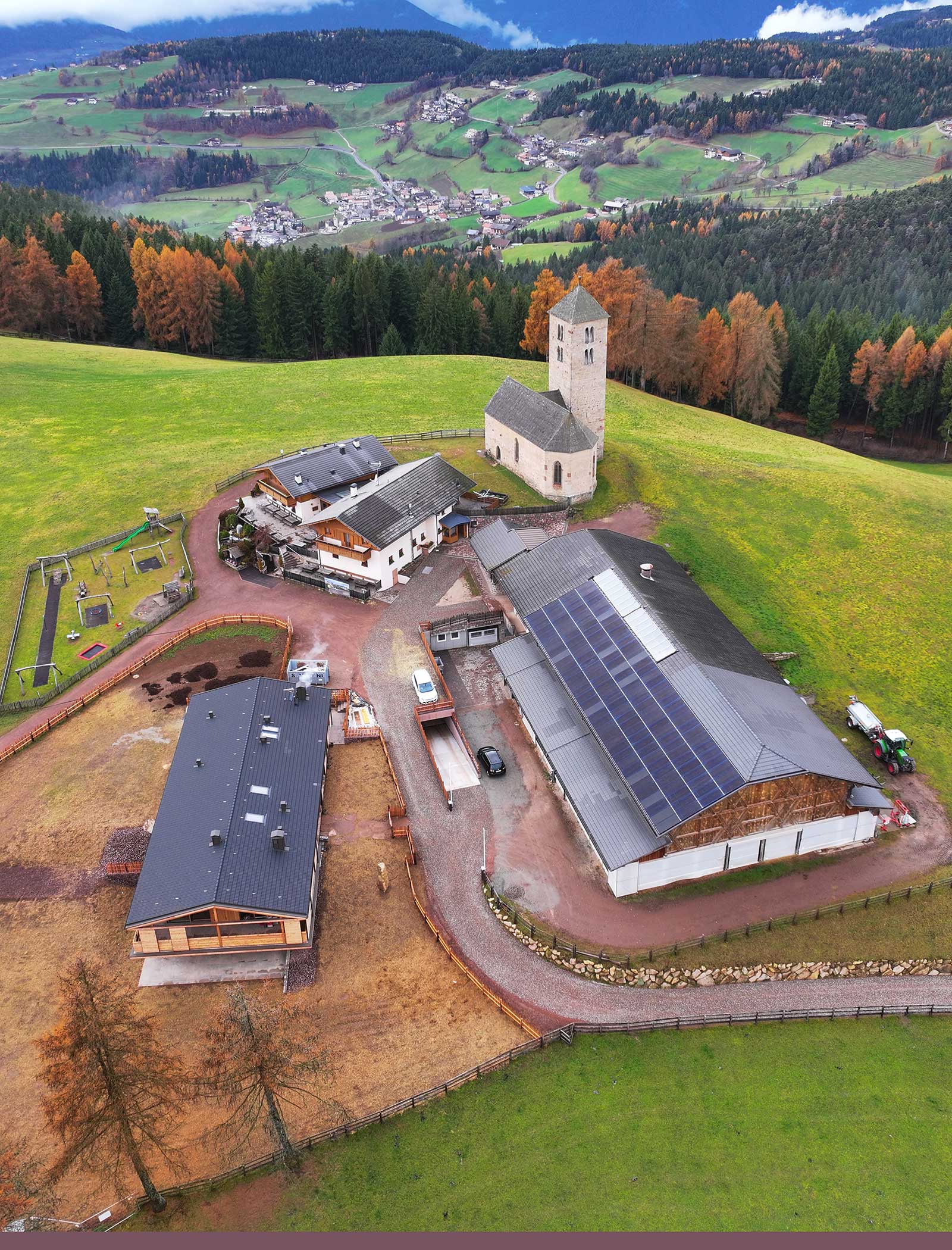 Luftaufnahme eines ländlichen Bauernhofs mit mehreren Gebäuden, einer Kirche, Sonnenkollektoren und grünen Feldern. - Langfennhof