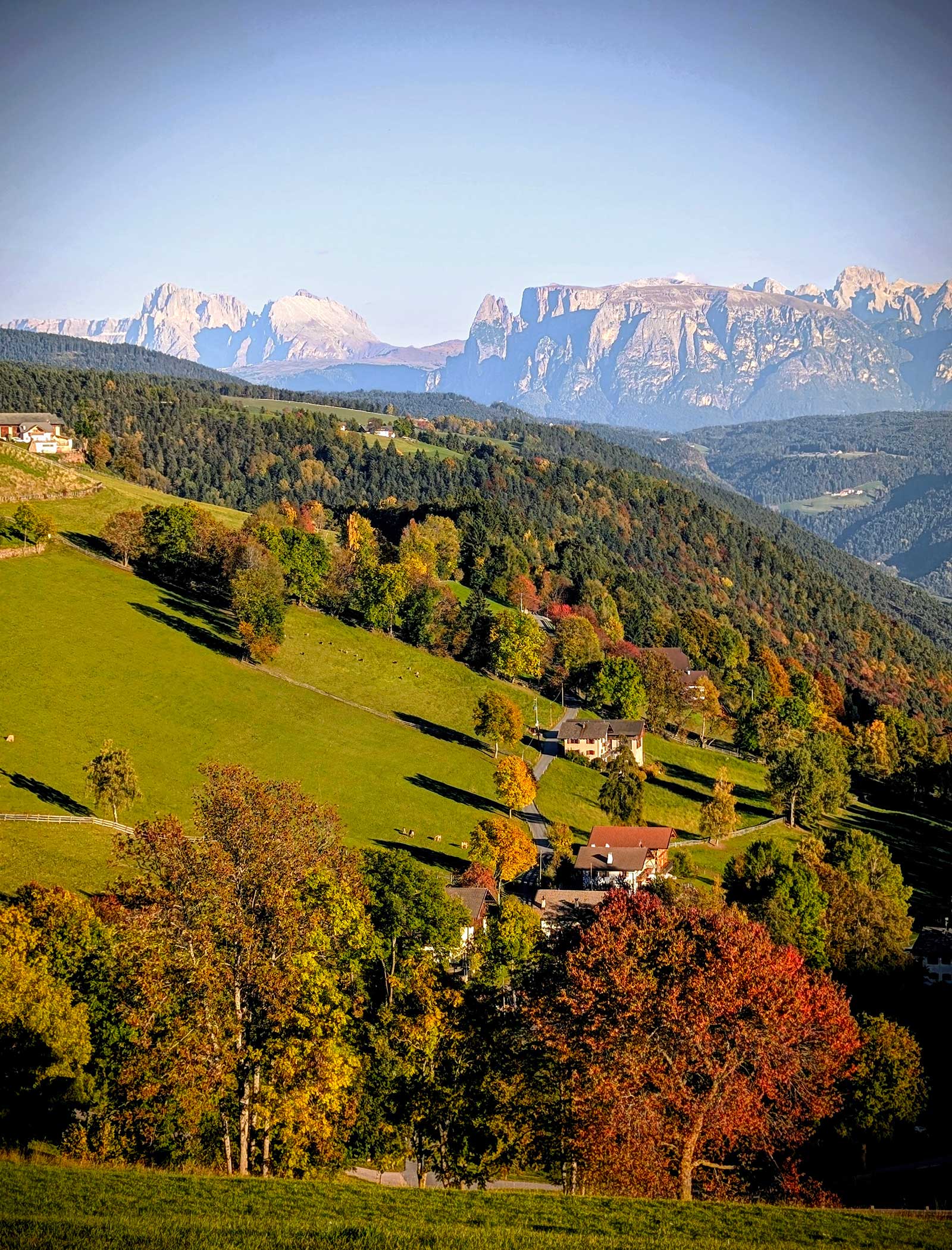 Sanfte, grüne Hügel mit verstreuten Häusern, bunte Herbstbäume und ferne Berge unter einem klaren Himmel. - Langfennhof