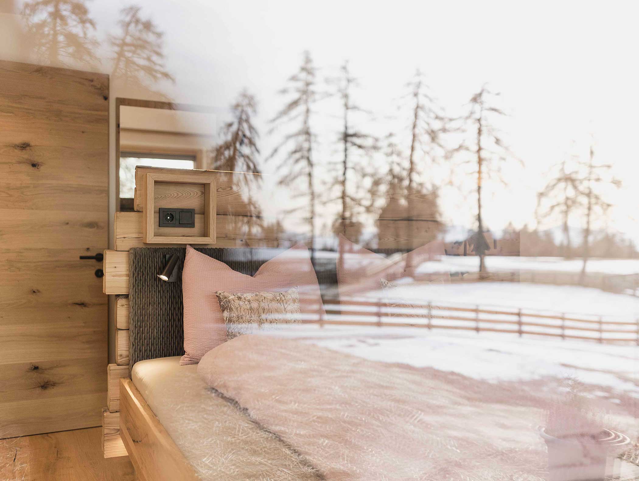 Gemütliches Holzschlafzimmer mit einem Bett und einem großen Fenster mit Blick auf verschneite Bäume und eine friedliche Szene im Freien. - Langfennhof