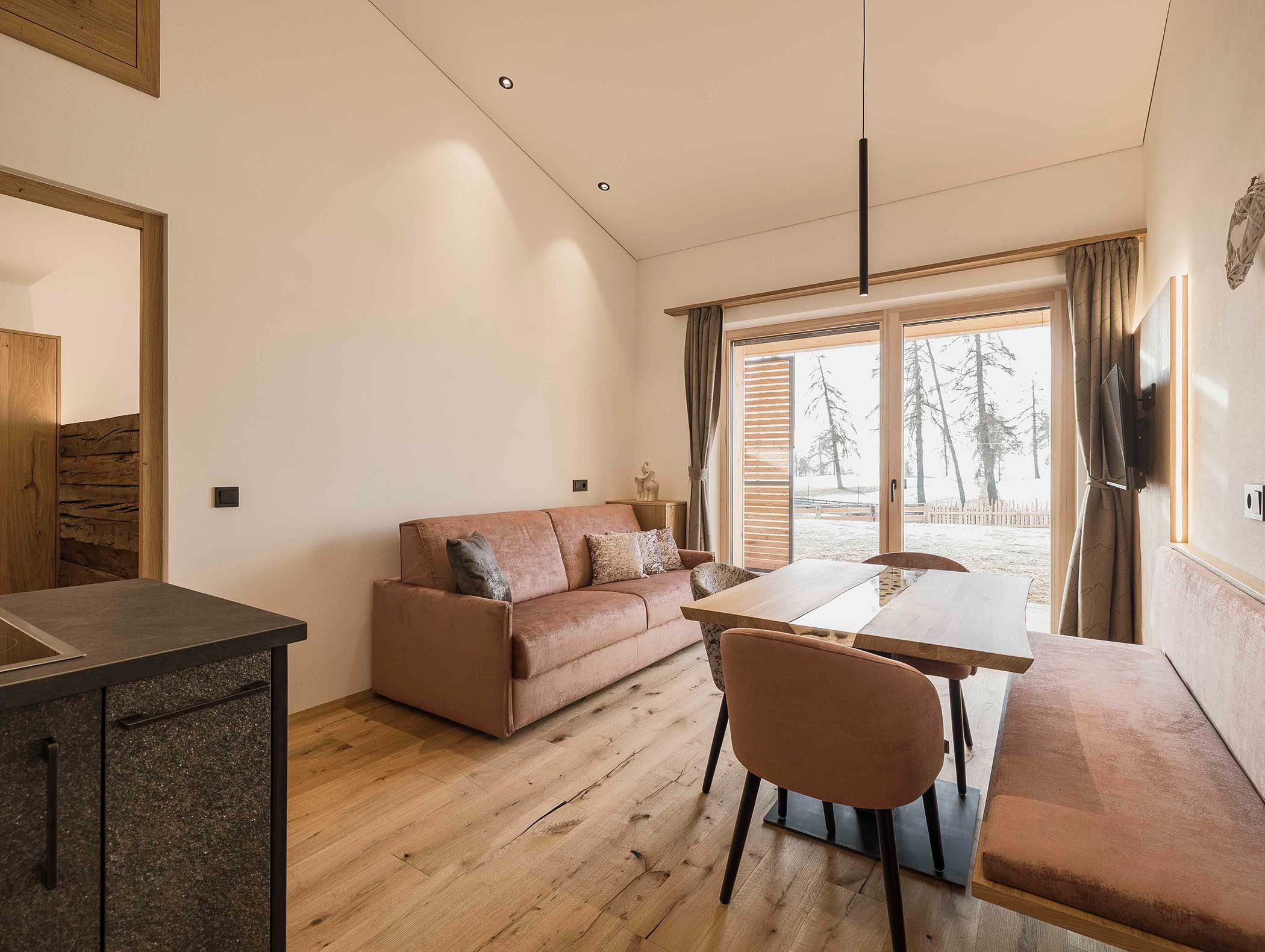 Moderner, gemütlicher Wohn- und Essbereich mit Sofa, Holztisch, Stühlen und großem Fenster mit Blick ins Freie. - Langfennhof