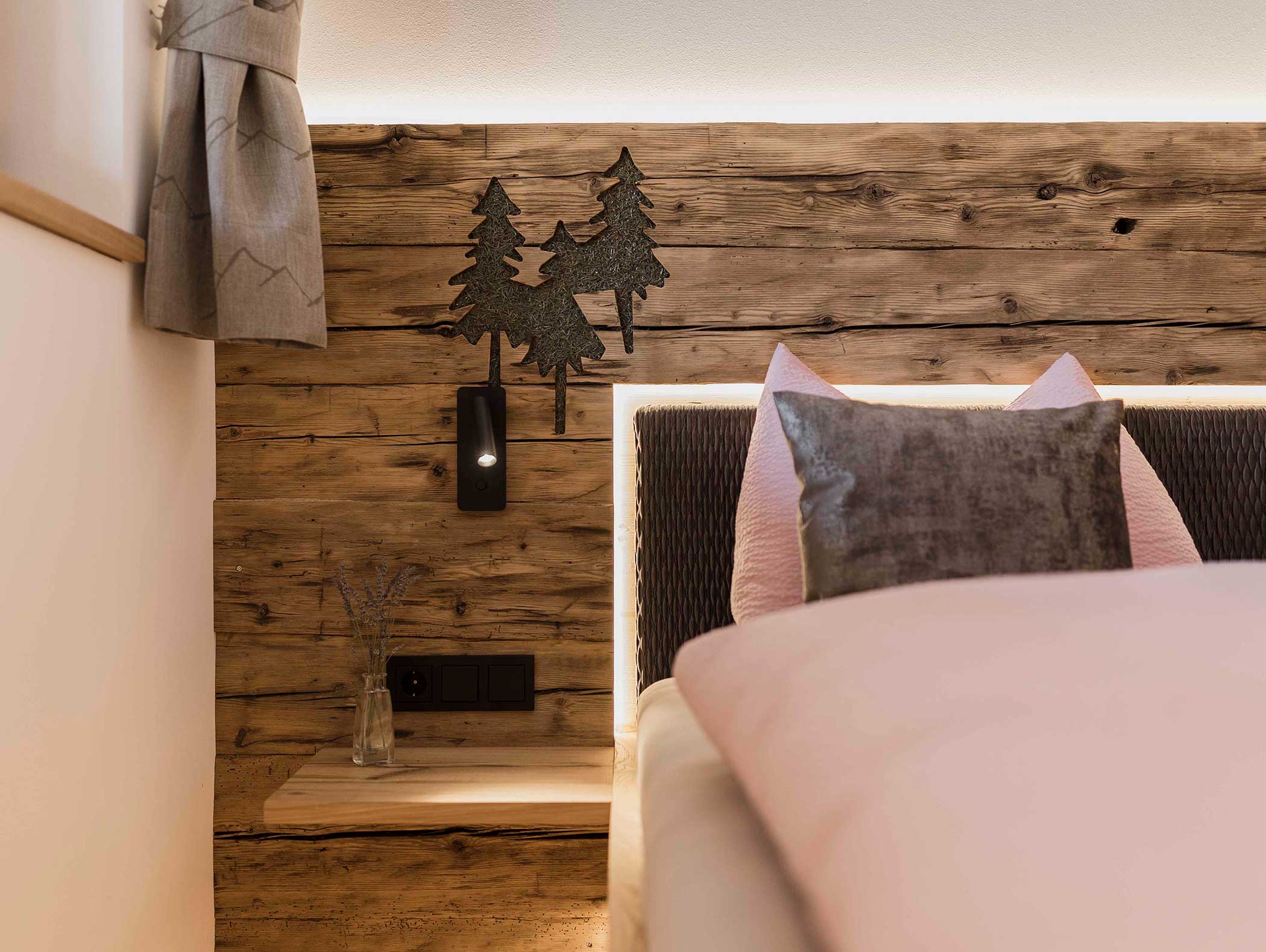 Gemütliches Schlafzimmer mit rustikalem Holzkopfteil, Baumdekoration aus Metall und einem Nachttisch mit einer kleinen Vase. - Langfennhof