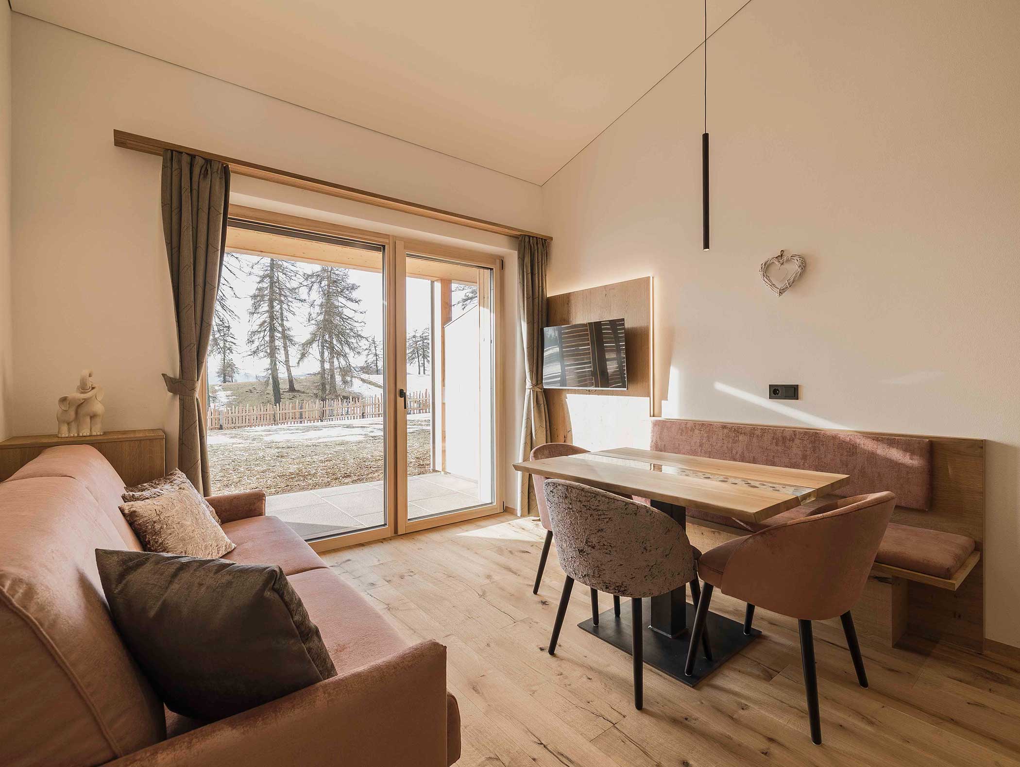 Gemütlicher Wohn-Essbereich mit Sofa, Tisch, Stühlen, TV und großen Glastüren, die auf eine Terrasse mit Aussicht führen. - Langfennhof