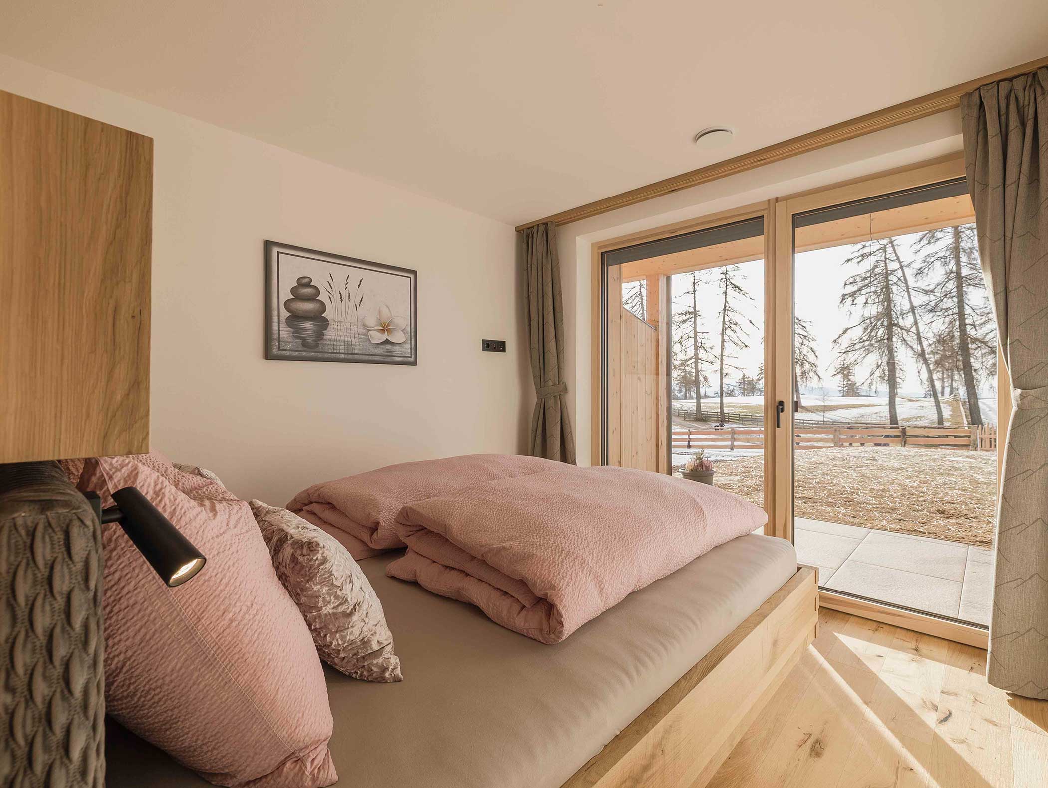 Gemütliches Schlafzimmer mit rosa Bettwäsche, großem Fenster und Blick auf Bäume und Terrasse. - Langfennhof
