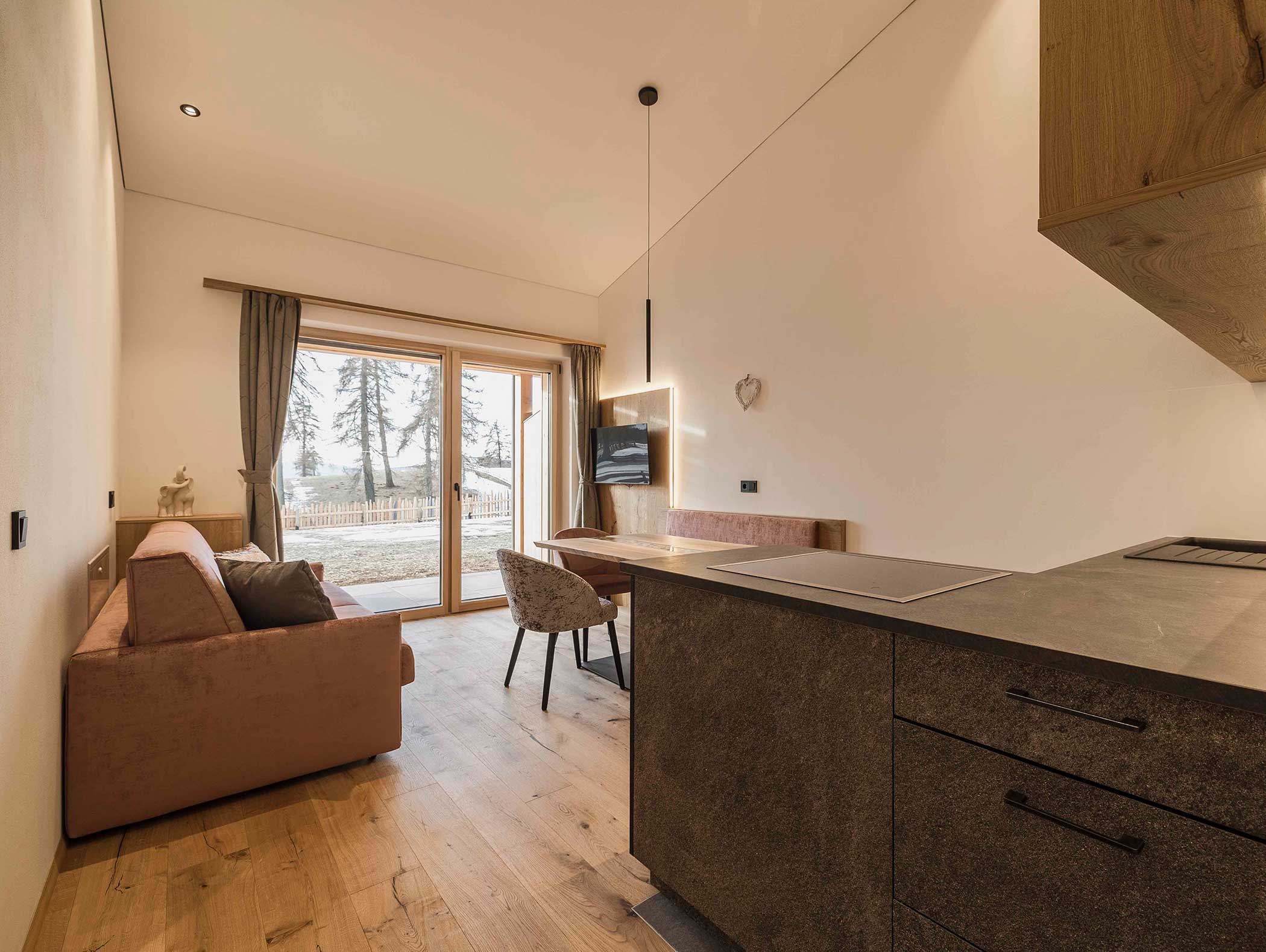 Modernes Studio mit Holzfußboden, Sofa, Esstisch, TV und großen Glastüren mit Blick auf Bäume. - Langfennhof