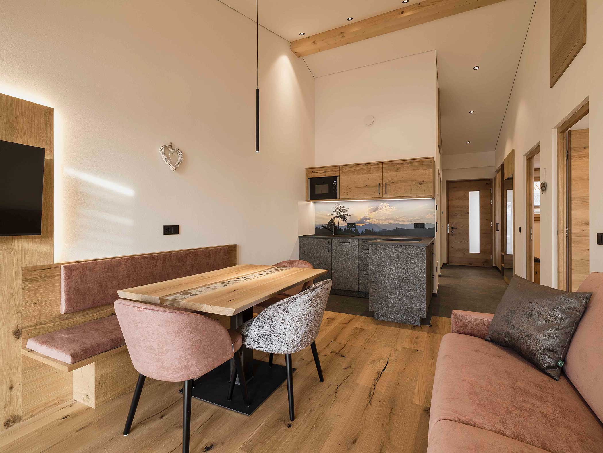 Modernes, gemütliches Apartment mit Holzakzenten, einem Esstisch, rosa Stühlen und einer Küchenzeile in warmer Beleuchtung. - Langfennhof