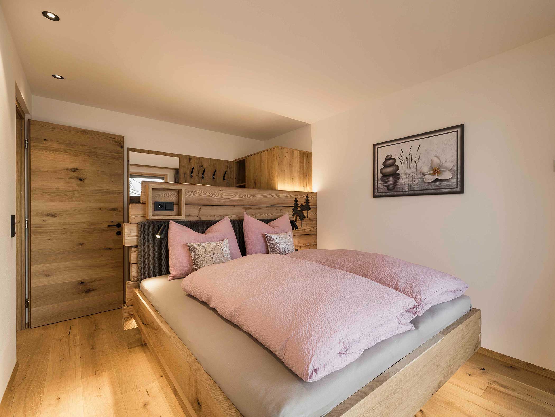 Gemütliches Schlafzimmer mit einem Holzbett, rosafarbener Bettwäsche, Holzmöbeln und einer Wandmalerei zum Thema Natur. - Langfennhof