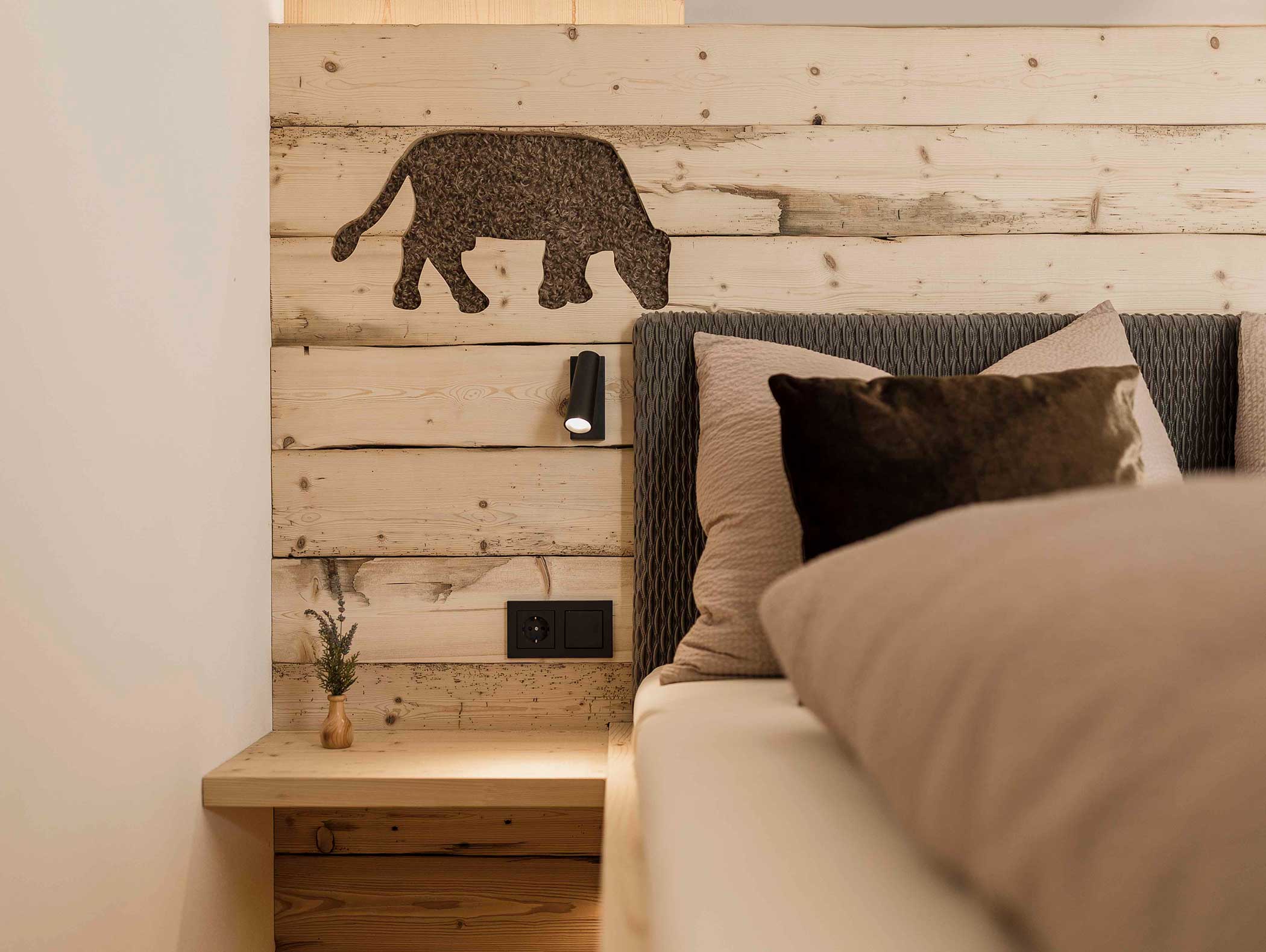 Gemütliches Schlafzimmer mit Holzkopfteil, kleiner Bärensilhouette, Nachttischlampe und neutraler Bettwäsche. - Langfennhof