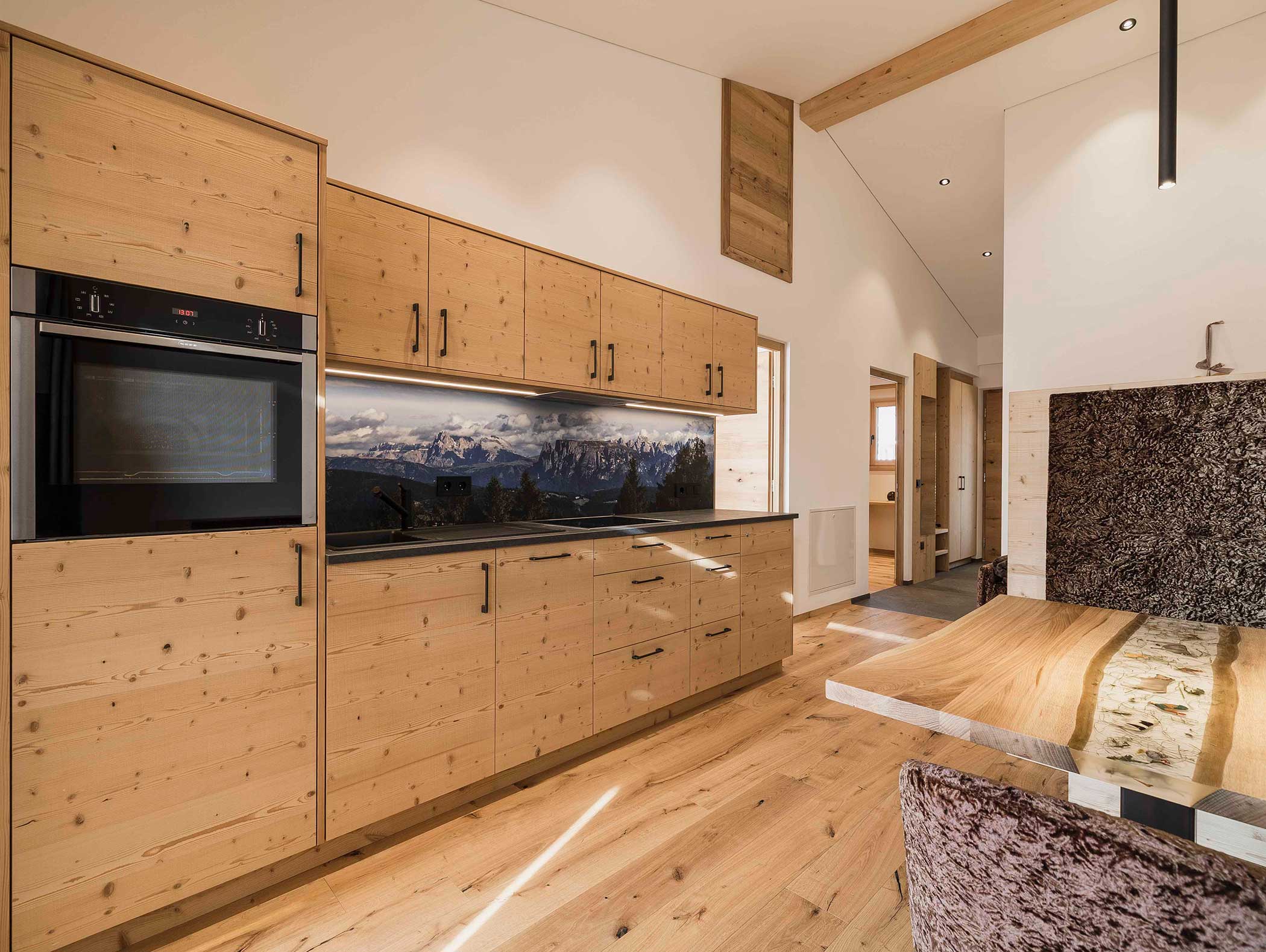 Moderne Küche mit hellen Holzschränken, schwarzen Geräten und einer Aufkantung mit Bergmotiven. - Langfennhof