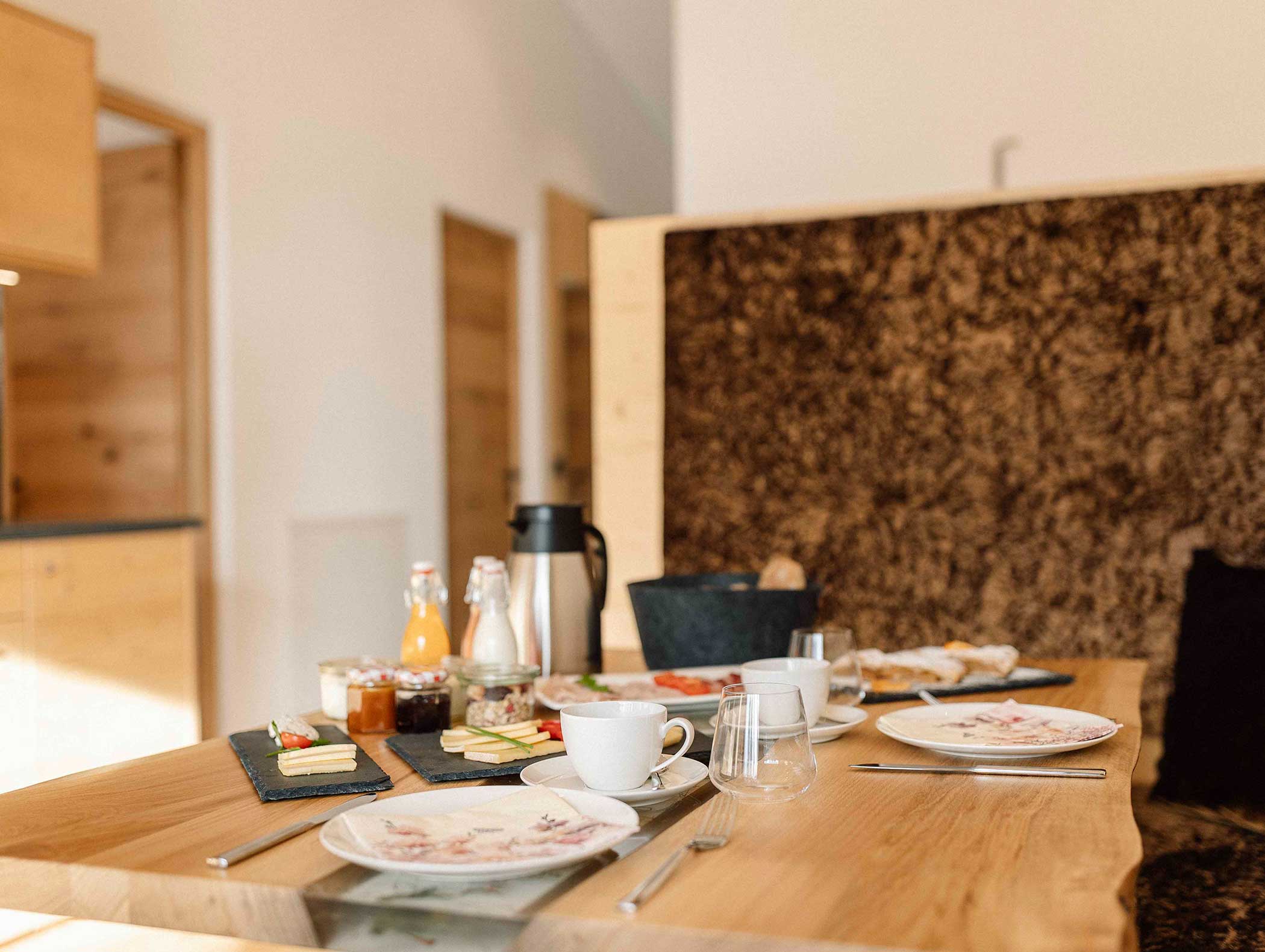 Der Frühstückstisch ist mit Tellern, Tassen, Saft, Milch, Käse und Gebäck in einer gemütlichen Essecke gedeckt. - Langfennhof