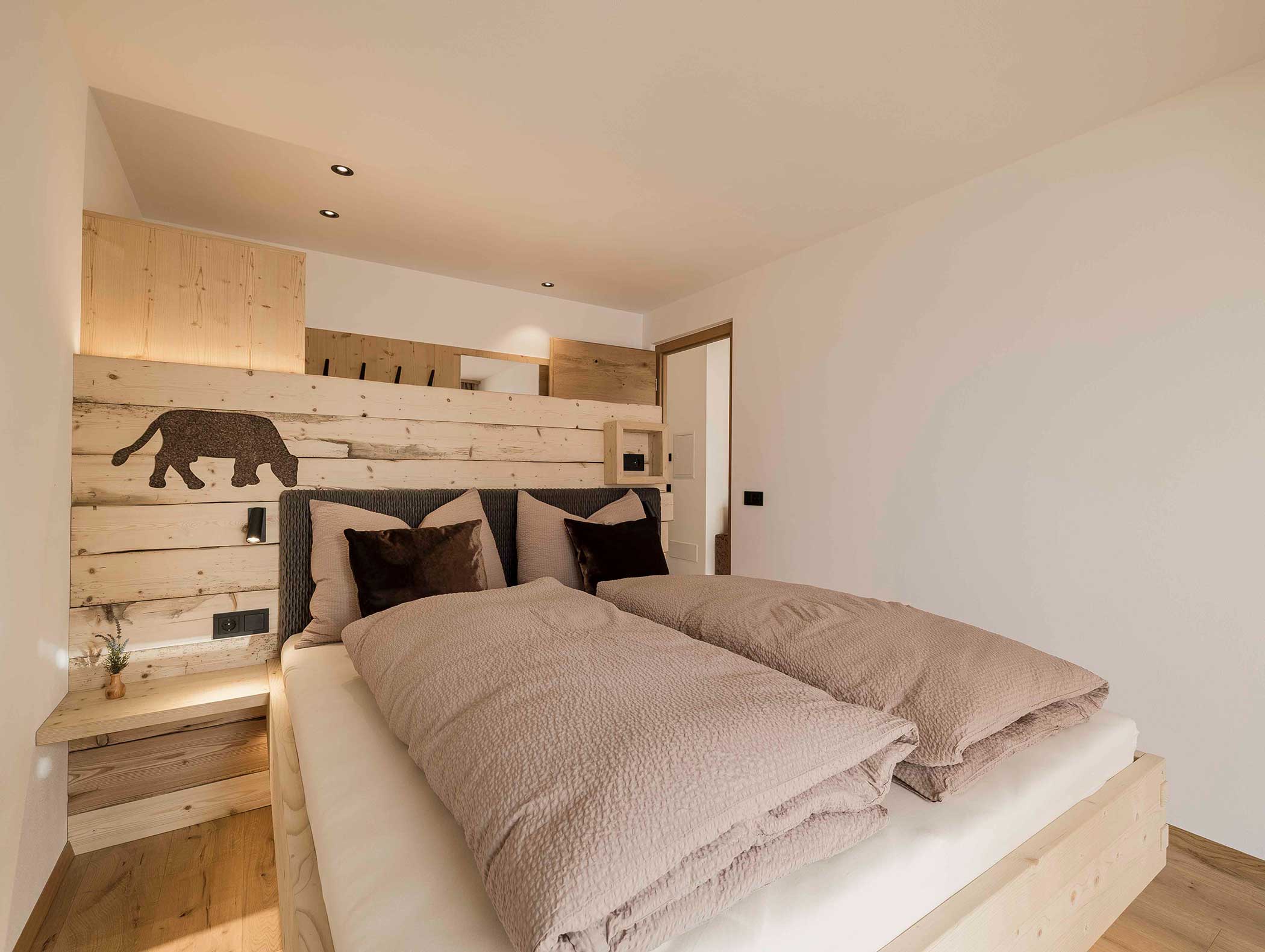 Gemütliches Schlafzimmer mit Holzdekor, einem Doppelbett und einer schwarzen Tiersilhouette auf dem Kopfteil. - Langfennhof